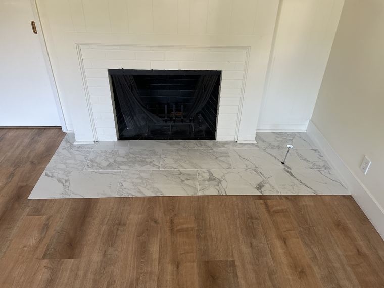 An interior fireplace with a marble hearth meeting a newly laid wood floor.