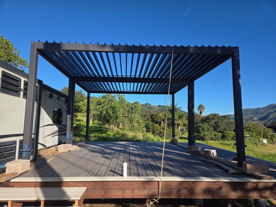 A black louvered pergola standing over a new deck, open hills in the distance.