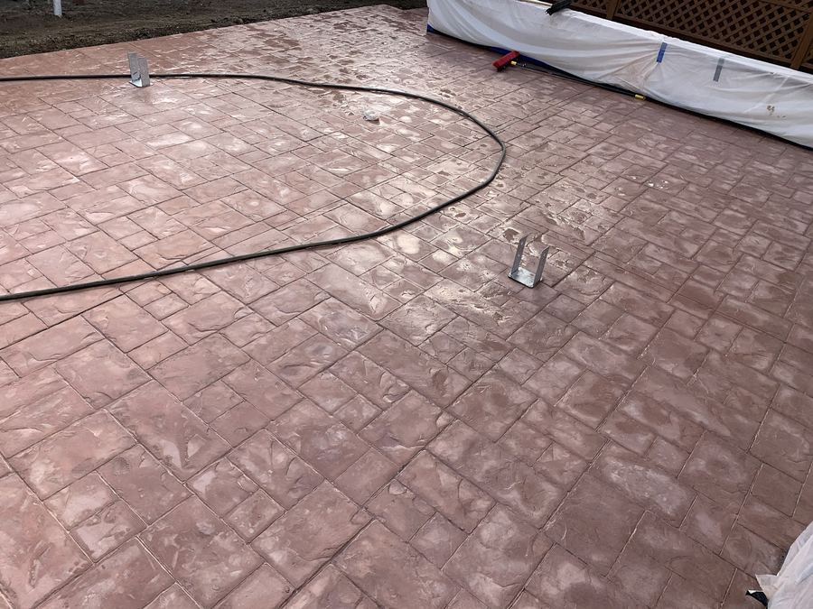 A stamped concrete patio in a soft red-brown, freshly finished and still being worked on.