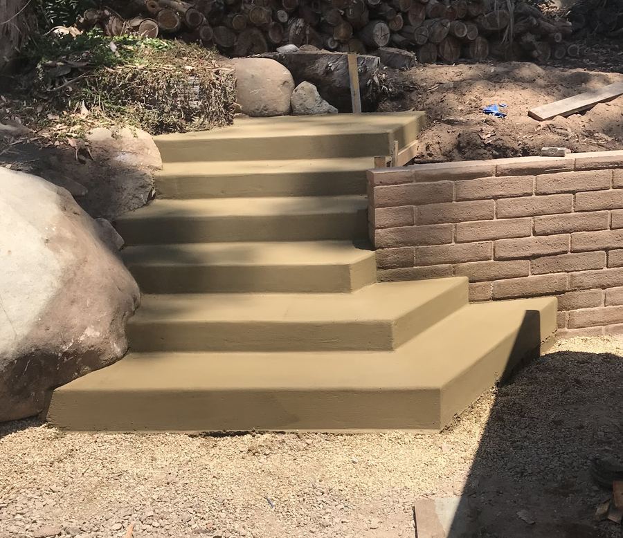 Poured concrete steps running down a slope beside a tan block retaining wall.