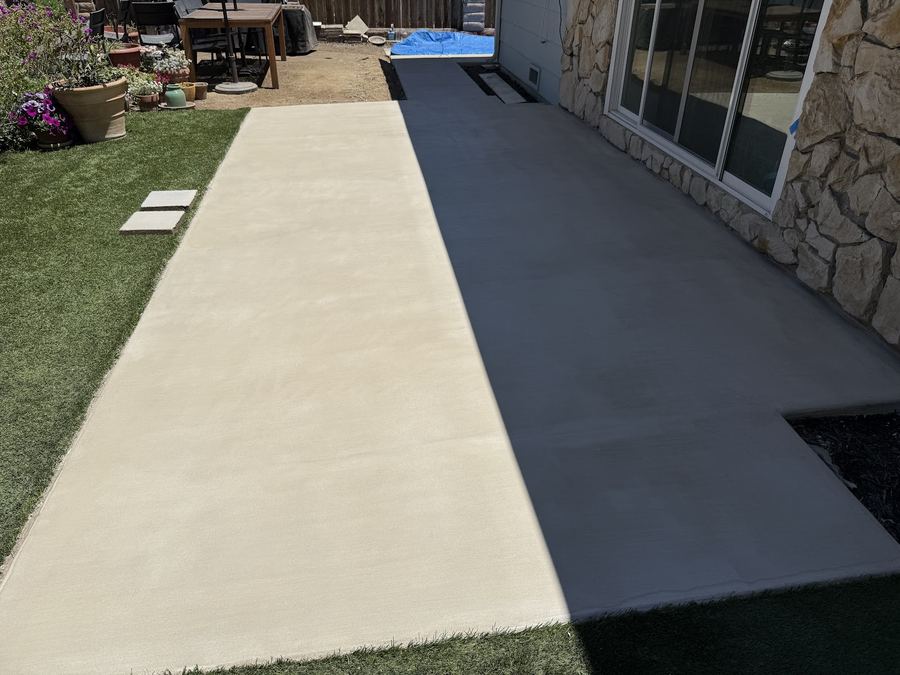 A long concrete walkway running between a stone-faced house and a strip of lawn.